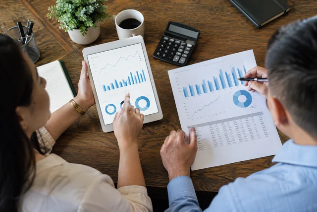 Two marketing analysts comparing campaign conversion charts on a tablet and printed performance report.