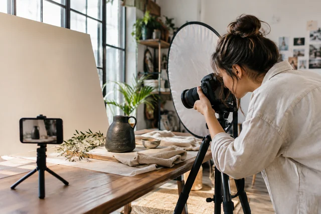 A content creator photographing a ceramic product in a small daylight studio with camera.